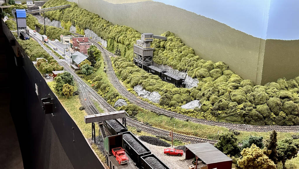 A model railroad layout with lush green sceneery and an industrial line in the center of the image running from top left to bottom right