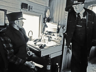 Black & white photo of conductor and brakeman by desk in caboose.