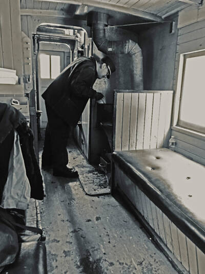 Black & white photo of brakeman tending fire in caboose stove.