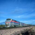 An Amtrak passenger train rolls through arid country against a blue sky