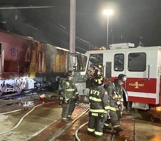 Fire truck with fire-damaged locomotive in background