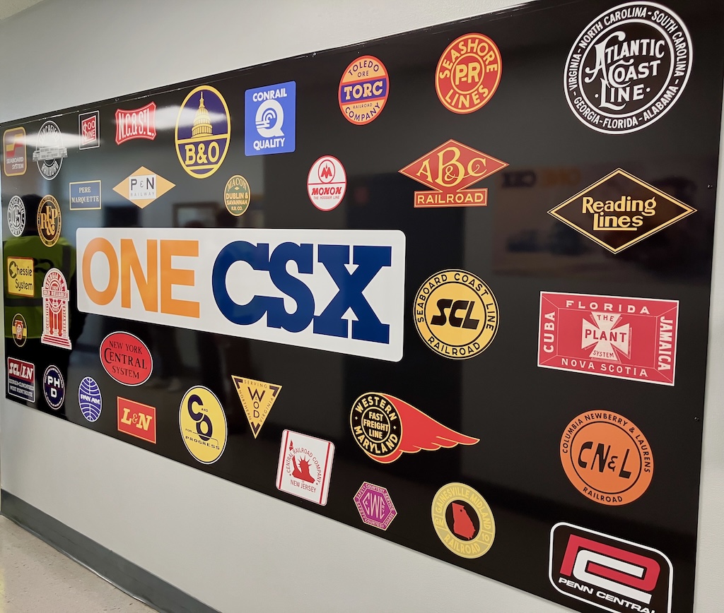 Board with railroad logos on wall of CSX facility