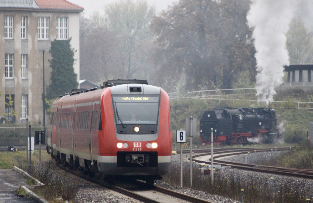 Red DMU passenger train with steam engine in background