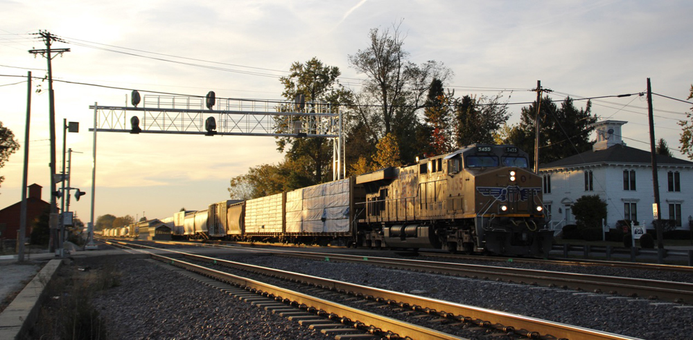 Train passing under signal bridge at sunset