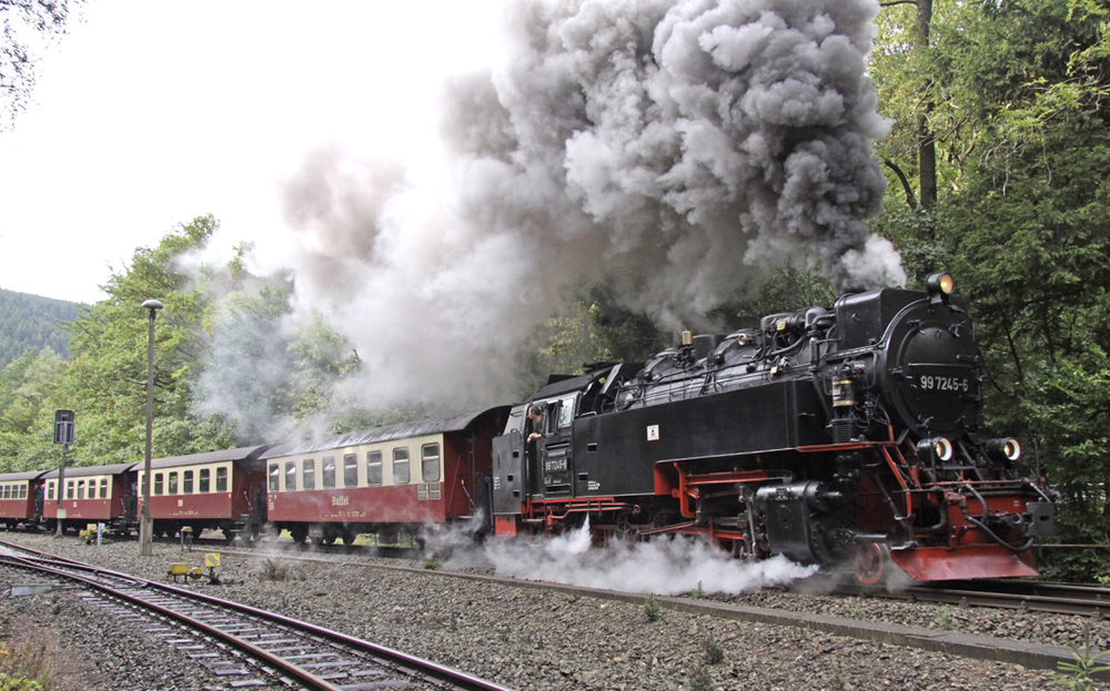 Steam engine under large plume of smoke with passenger cars