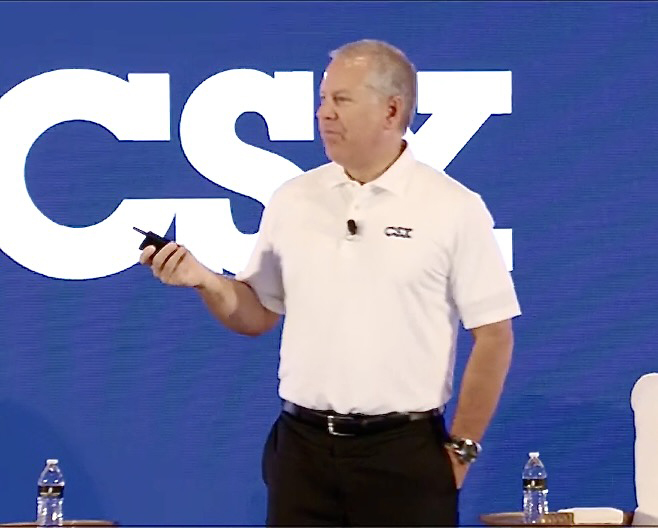 Man in white polo shirt speaking in front of CSX backdrop