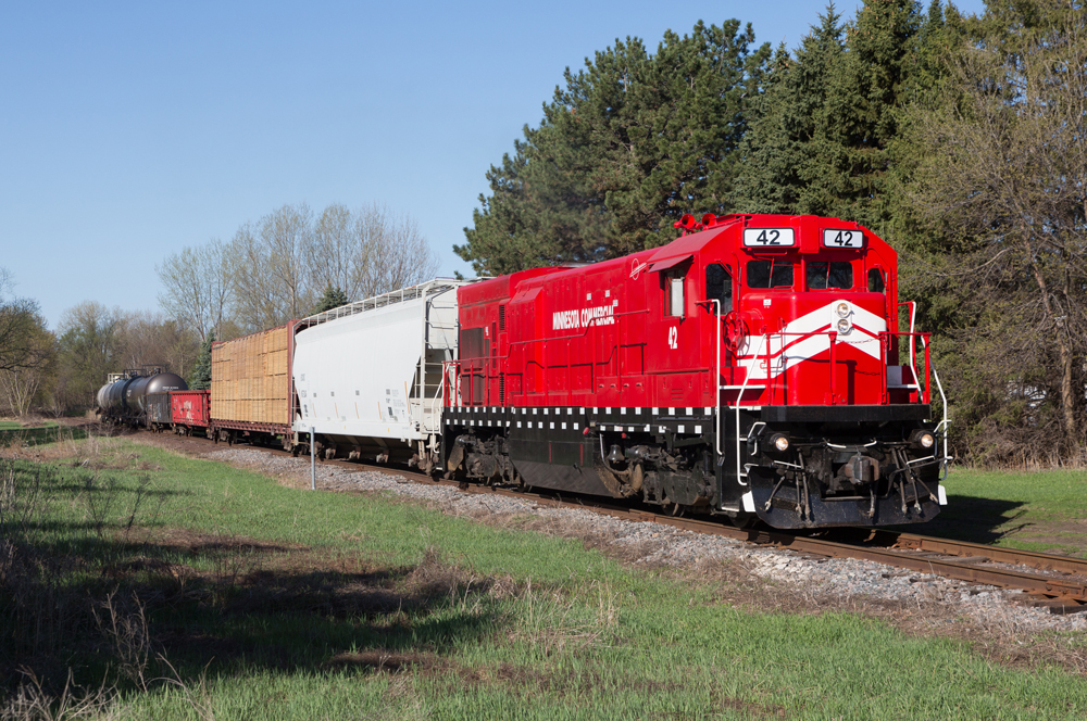 Red locomotive with white nose strips and short string of freight cars