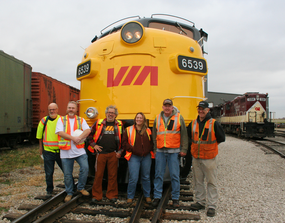 Front view of yellow and blue locomotive with people standing in front