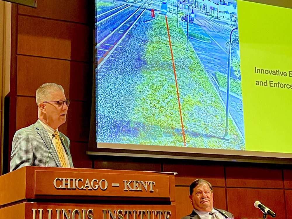 Man speaking at podium with image on screen in background