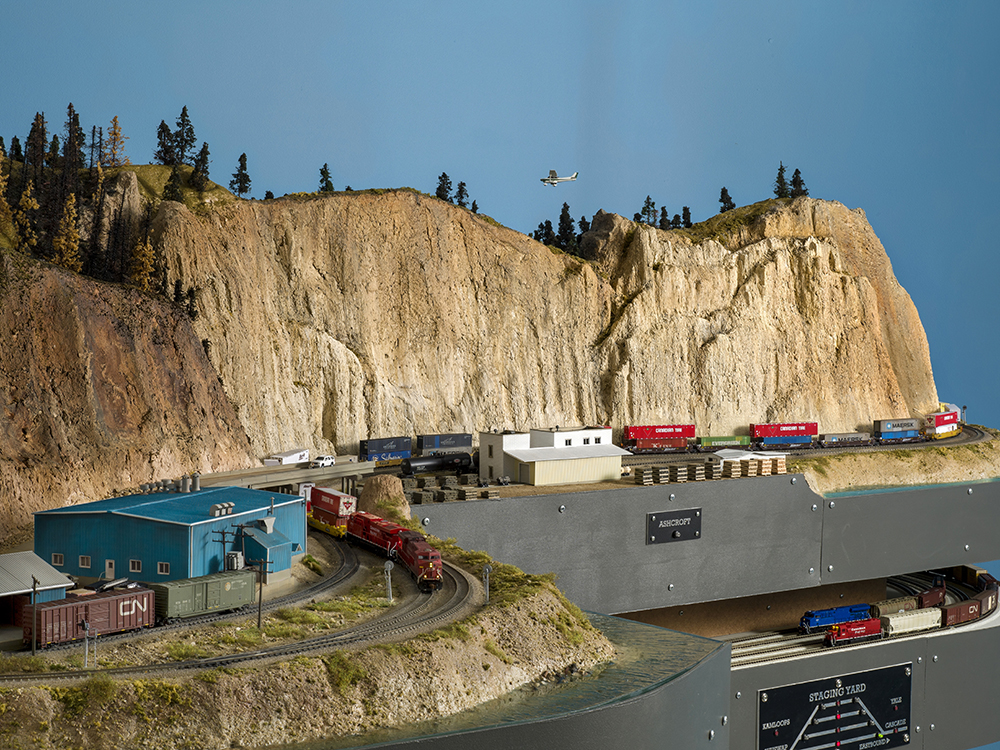 tall rugged brown mountains set against a blue sky dwarf model trains running below them on a toy train layout. 