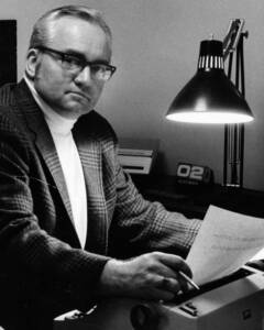 Man with glasses and jacket holding paper under lamp