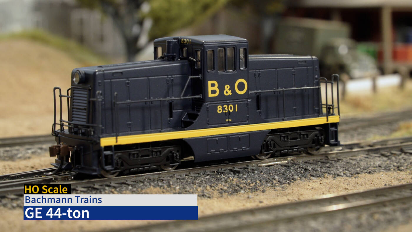 Screen capture showing GE 44-ton switcher in blue and yellow paint on scenicked layout with product description in lower left corner.