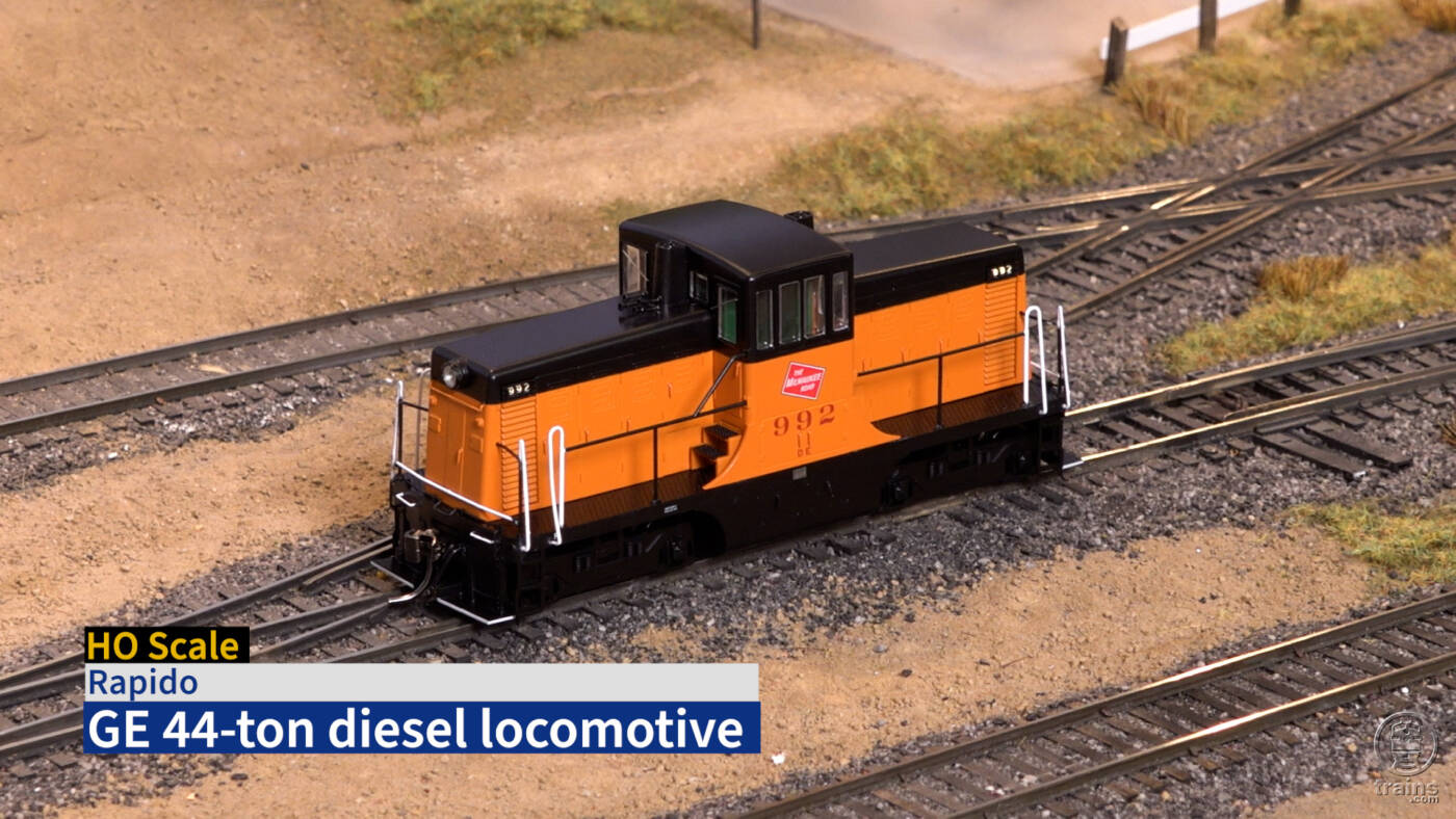 Title screen of video with identification bar in lower left corner and HO scale locomotive painted orange and black on scenicked layout.