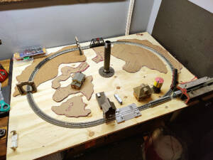 A plywood train table with an N scale sectional track oval surrounded by pieces of cardboard