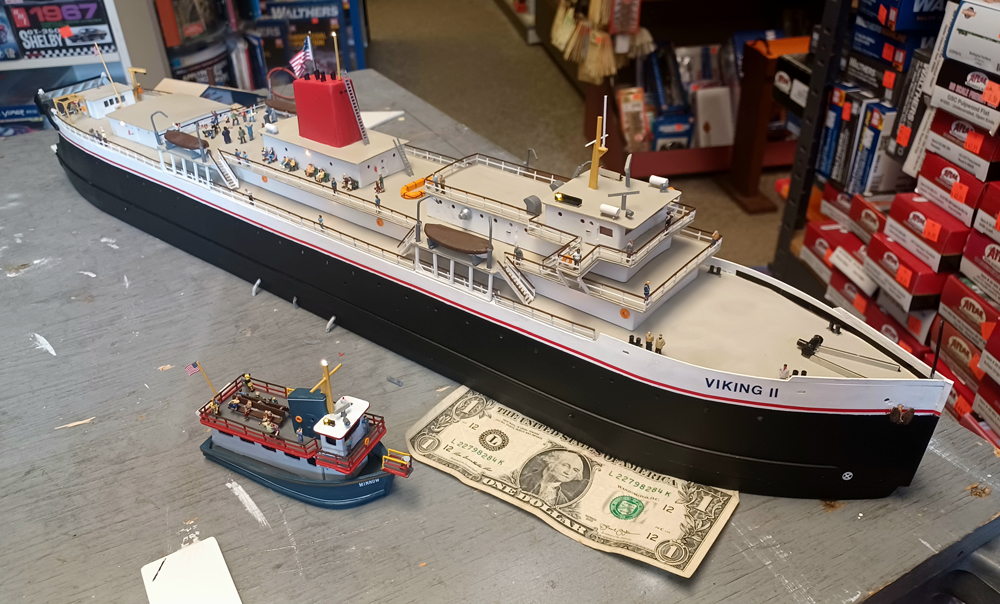 Color photo of N scale carferry and tourist boat on gray plywood with one dollar bill for scale reference.