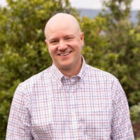 A photograph of Craig Fuller in a button down shirt in front of a bank of trees