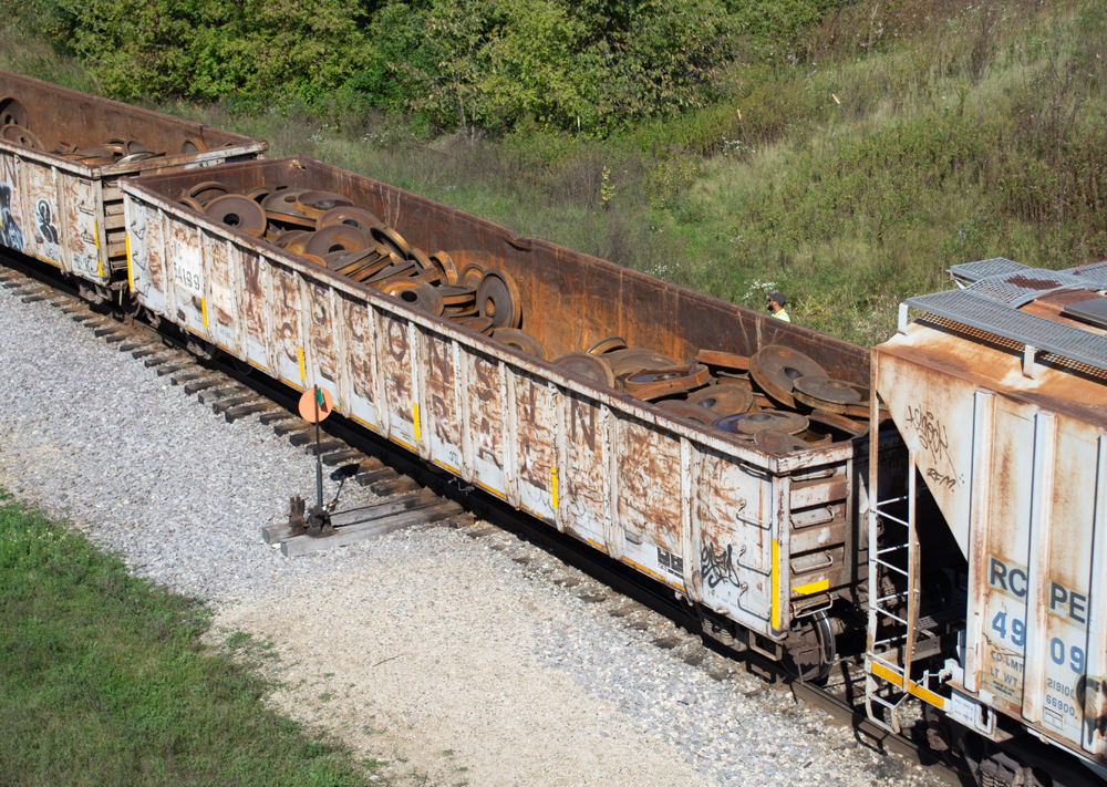 Color photo of gondola painted light gray with rusty wheels inside.