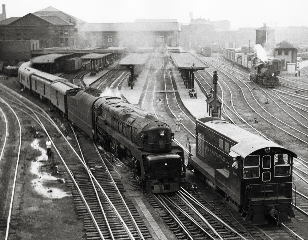 Black & white photo of a streamlined steam locomotive pulling a passenger train out of the station.