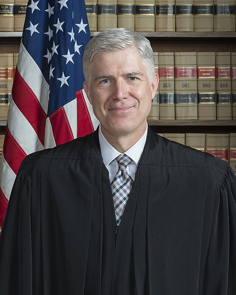 Man in black judge's robe standing in front of U.S. flag and law books