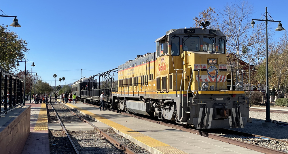 Yellow locomotive with two cars at station platform