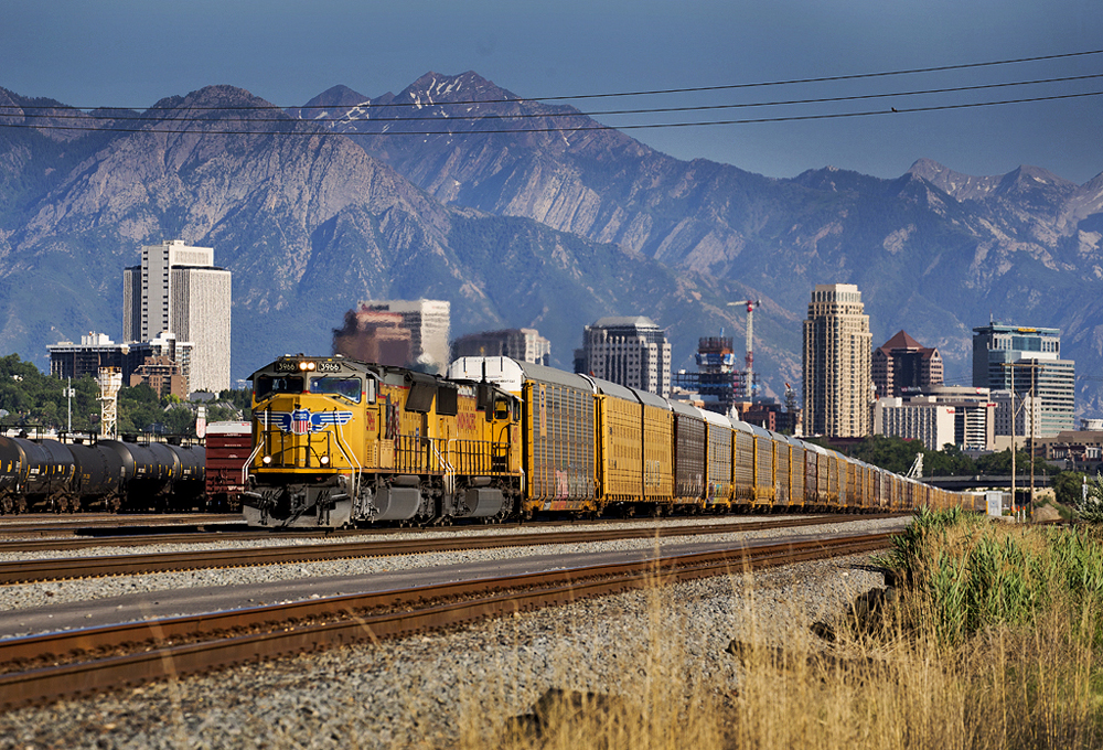 Yellow locomotives on freight train with city skyline and mountains in background