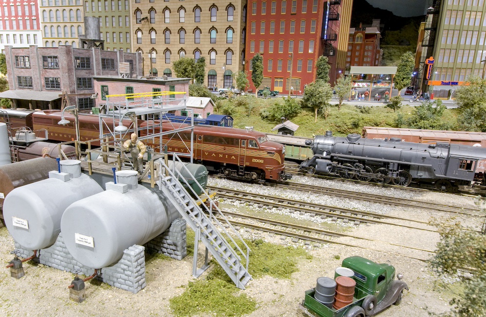 Large scale diesel passes by steam train on layout.