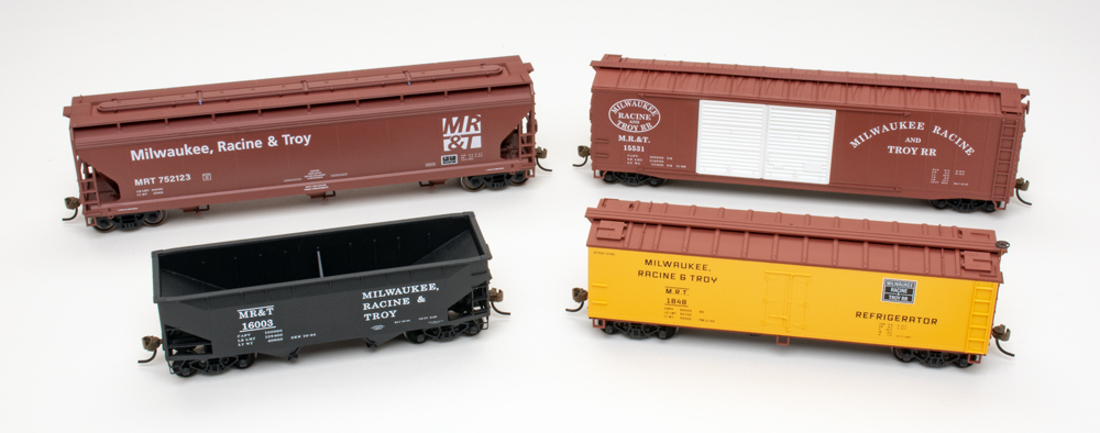 Color image of four HO scale freight cars in brown, black, and yellow paint on white background.