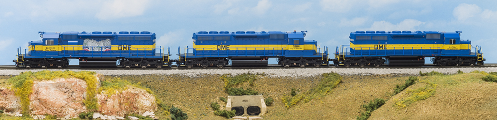 Photo of three HO scale diesel locomotives painted blue and yellow on scenicked base.