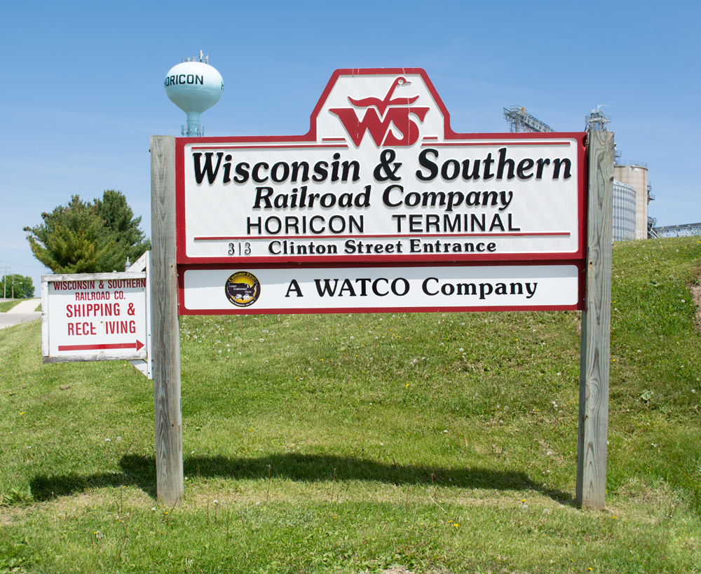 Color photo of red-and-white sign with black lettering mounted on wood posts.