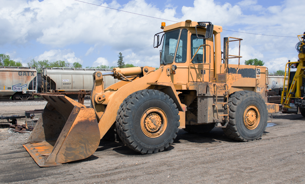 Color photo of yellow front-end loader with covered hoppers in background