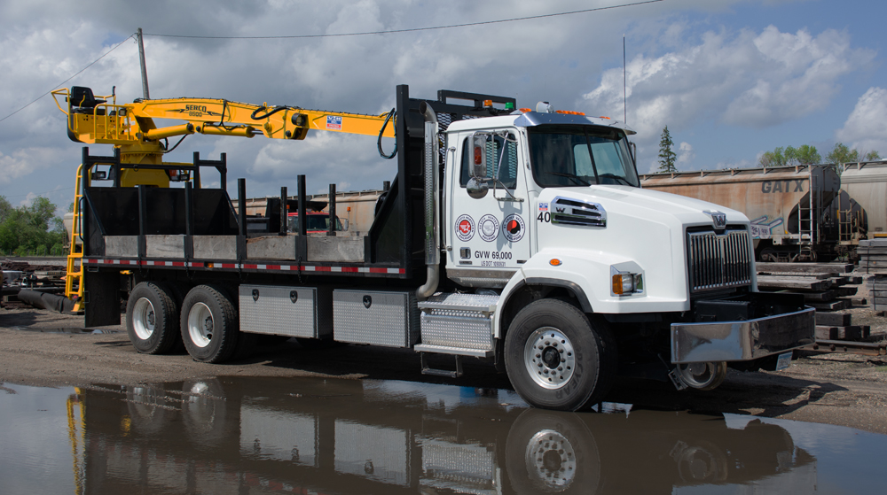 Color photo of white truck with black bed and yellow grapple