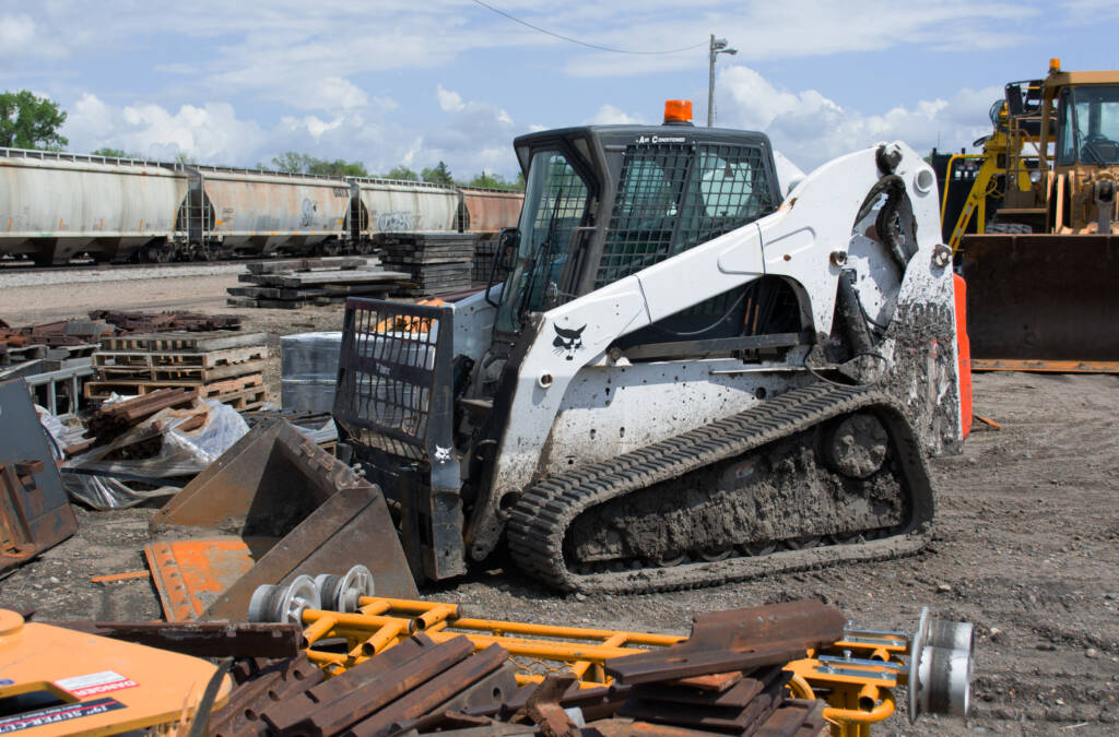 Color photo of tracked skid-steer in railroad yard. 