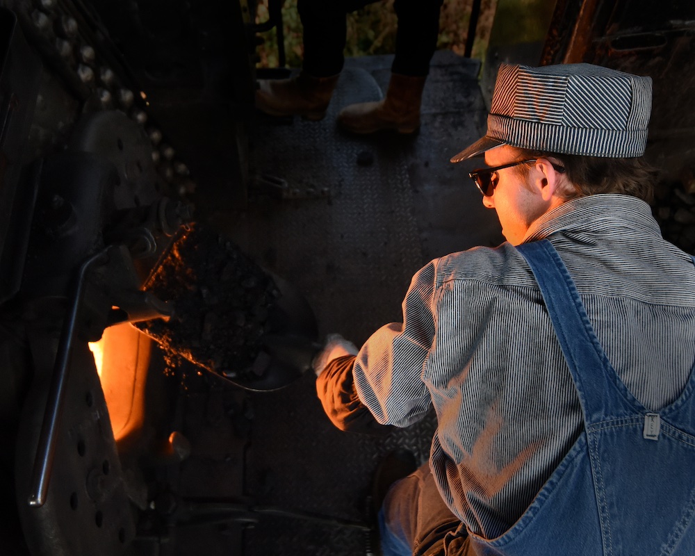 Young individual tends to a fire inside the cab of a steam locomotive.