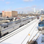 Passenger train passing through snow-covered yard with Chicago skyline in distance