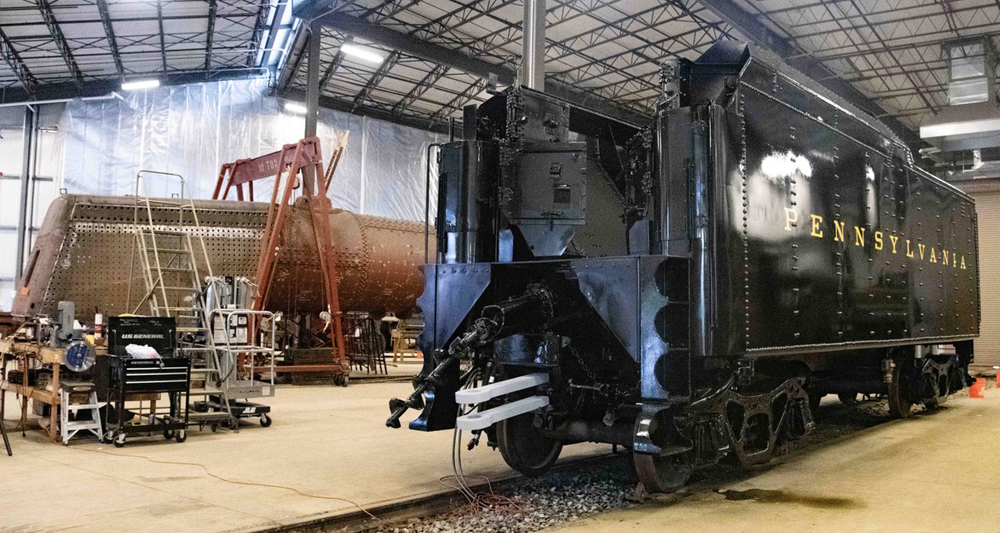 Steam locomotive tender in shop building with boiler of locomotive in background