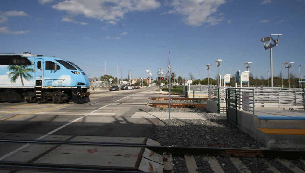 Locomotive of commuter train crosses street adjacent to station platforms