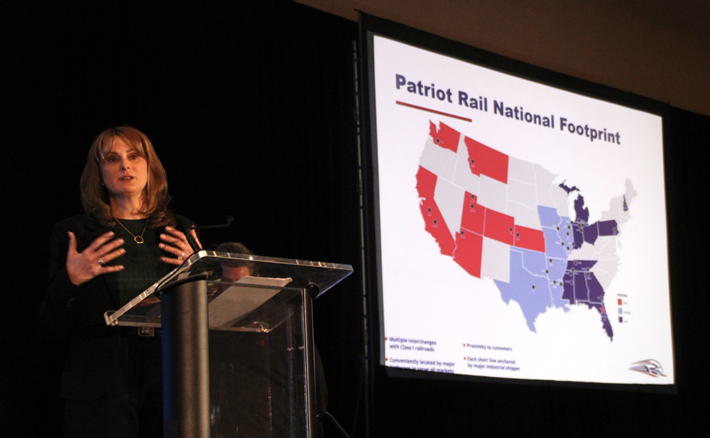 Woman at podium with slide of rail company's holdings in the background