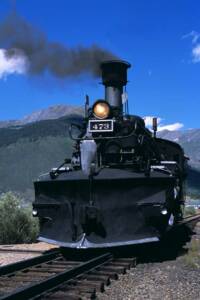 Low-angle photo of smoking black steam locomotive with large snow plow