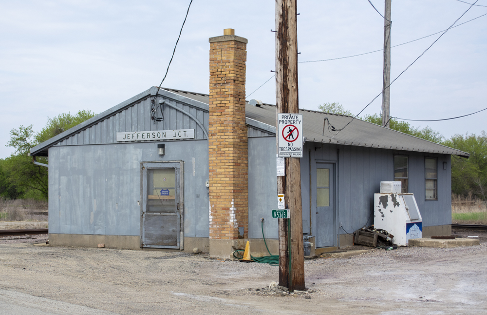 Color photo of gray metal building with doors, windows, and brick chimney.