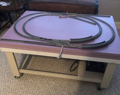 The beginning of a model railroad layout, with pink insulation foam and track on a wooden base