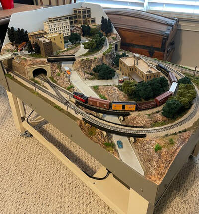 An N scale mini-layout is viewed at an angle, with tow model trains running parallel to one another