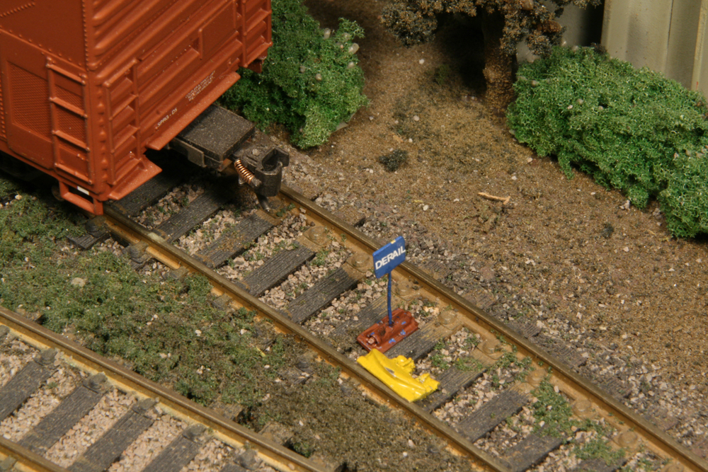 Color photo of HO scale track with boxcar, hinged derail, and blue sign.