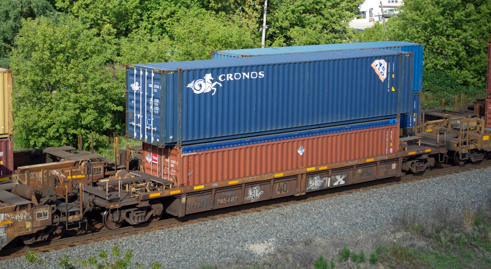 Color photo of weathered yellow well car with mineral red and blue intermodal containers.