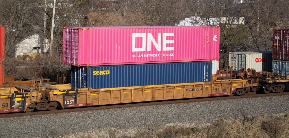 Color photo of weathered yellow well car with cherry blossom magenta and blue containers.