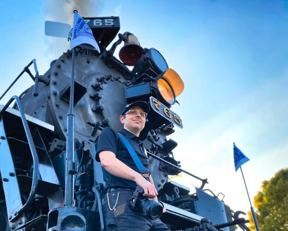 Young individual standing in front of a steam locomotive