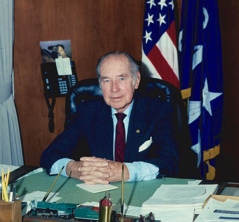 Man in suit siting at desk with flags in background