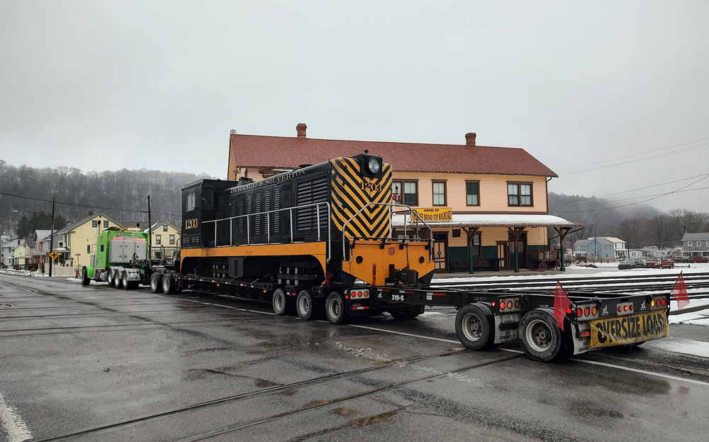 Diesel locomotive on flatbed truck with East Broad Top building in background