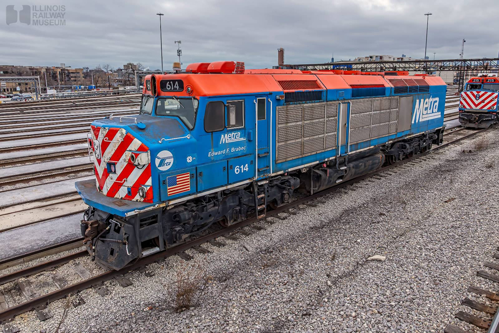 Blue and orange locomotive with steel side panels in rail yare