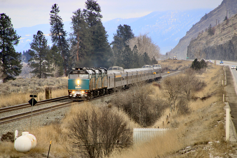 Passenger train with dome cars on straight next to highway