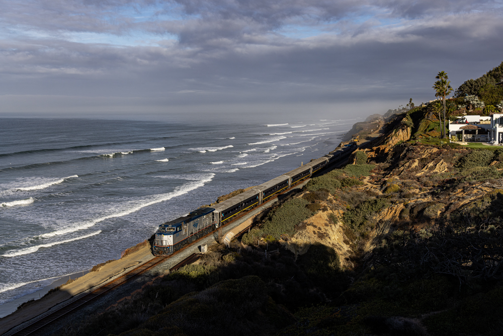 Passenger train in morning light running next to ocean